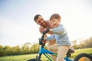 Trying the bicycle., Happy father with son are having fun on the field at summertime photo