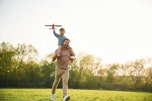 Orange colored toy plane, ,playing. ,,Happy father with son are having fun on the field at summertime photo