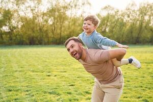 Sitting on man's shoulders. Happy,, father with son are having fun on the field at summertime photo