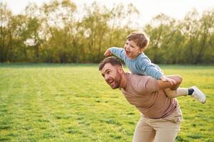 Sitting on man's shoulders., Happy father with son are having fun on the field at summertime photo