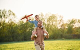Orange colored ,toy,plane, ,playing. Happy father with son are having fun on the field at summertime photo