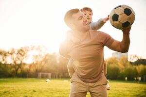 On ,shoulders, with, soccer ball. Happy father with son are having fun on the field at summertime photo