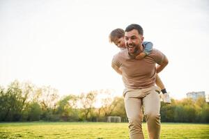 Wellbeing, kid is ,on, the ,shoulders or back. Happy father with son are having fun on the field at summertime photo