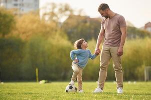 Teaching how to play a ,,soccer. Happy father with son are having fun on the field at summertime photo
