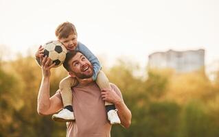On shoulders, with, soccer ball. Happy father with son are having fun on the field at summertime photo