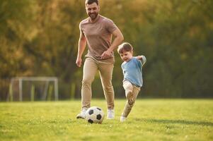 Teaching, how ,,to play a soccer. Happy father with son are having fun on the field at summertime photo