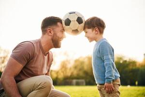 Soccer ball, holding, it by heads, fun. Happy father with son are on the field at summertime photo