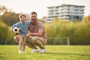 Sitting,,, holding soccer ball. Happy father ,with son are having fun on the field at summertime photo