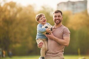 Standing, holding soccer ball. Happy father with son are having fun on the field at summertime photo
