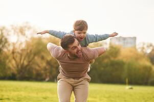 Sitting on man's ,shoulders. Happy father with son are having fun on the field at summertime photo