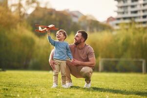 Weekend activities. Playing ,with ,toy plane. Happy father with son are having fun on the field at summertime photo