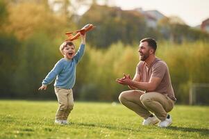 Weekend activities. Playing with toy plane... Happy father with son are having fun on the field at summertime photo