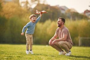 Weekend activities. Playing ,with, toy, plane. Happy father with son are having fun on the field at summertime photo