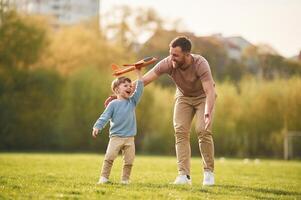In casual ,clothes. Running, with, toy plane. Happy father with son are having fun on the field at summertime photo
