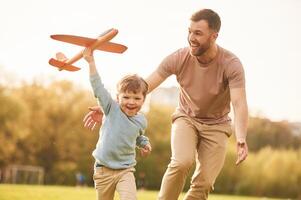 Summertime ,happiness. Running with, toy plane. Father with son are having fun on the field photo