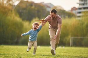 Flying high, holding toy plane, running.,, Happy father with son are having fun on the field at summertime photo