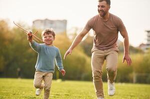 In ,casual ,clothes. Running with toy plane. Happy father with son are having fun on the field at summertime photo