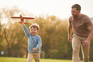 Summertime,, happiness. Running with toy plane. Father with son are having fun on the field photo