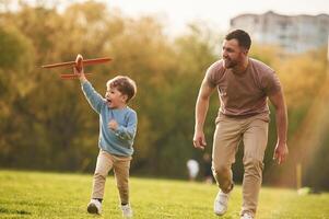 Summertime, happiness. Running with toy plane. Father with son are having fun on the field photo