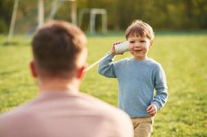 White ,paper ,cup telephone. Happy father with son are having fun on the field at summertime photo