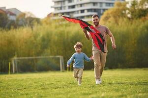 Beautiful red,, kite. Happy father with son are having fun on the field at summertime photo