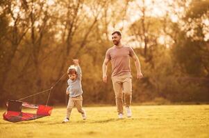 Beautiful ,red kite.. Happy father with son are having fun on the field at summertime photo