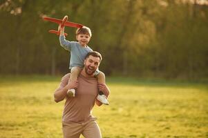 Flying high, holding,, toy plane, running. Happy father with son are having fun on the field at summertime photo