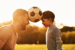 Positive emotions, holding soccer, ball ,by heads. Happy father with son are having fun on the field at summertime photo