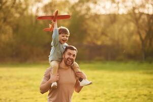 Flying high, holding ,toy plane, running. Happy father with son are having fun on the field at summertime photo