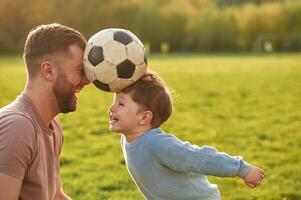 Positive, emotions, holding soccer ball by heads. Happy father with son are having fun on the field at summertime photo