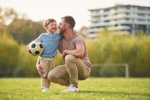 Sitting, holding soccer ,ball. Happy father with son are having fun on the field at summertime photo