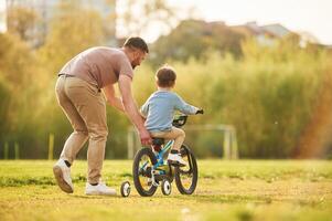 Riding ,on ,,the blue bicycle. Happy father with son are having fun on the field at summertime photo