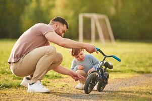Showing the parts of the bicycle. Happy father with son are having fun on the field at summertime photo