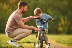 Riding on the ,,blue bicycle. Happy father with son are having fun on the field at summertime photo