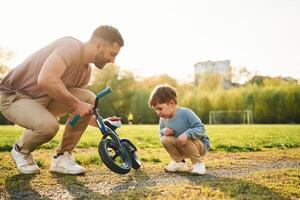 Little ,bicycle. Happy father with son are having fun on the field at summertime photo