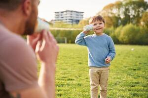 Using paper cup telephone. .Happy father with son are having fun on the field at summertime photo