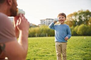 Using paper cup telephone. Happy ,father with son are having fun on the field at summertime photo