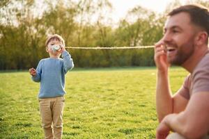 Talking by using paper ,cup telephone. Happy father with son are having fun on the field at summertime photo