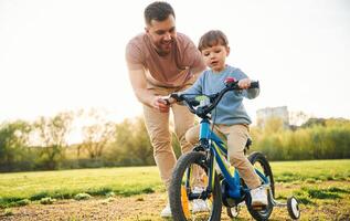 Trying the bicycle.. Happy father with son are having fun on the field at summertime photo