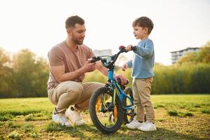Trying the bicycle. Happy,, father with son are having fun on the field at summertime photo