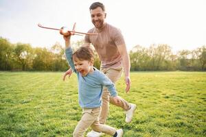Toy plane in, hand, running. Happy father with son are having fun on the field at summertime photo