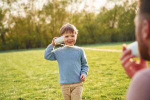 Using, paper cup telephone. Happy father with son are having fun on the field at summertime photo