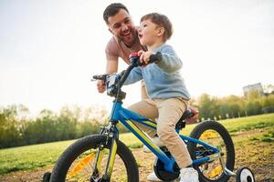 Trying ,,the bicycle. Happy father with son are having fun on the field at summertime photo