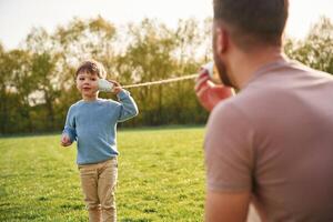 Using paper, cup telephone. Happy father with son are having fun on the field at summertime photo