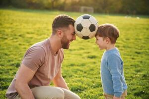 Soccer, ball, holding it by heads, fun. Happy father with son are on the field at summertime photo