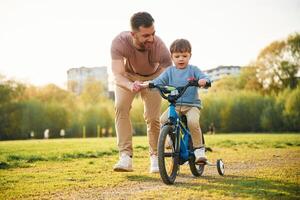 Riding on ,the blue bicycle. Happy father with son are having fun on the field at summertime photo