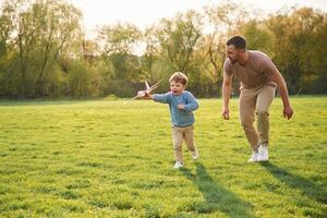 Toy plane in hand,, running. Happy father with son are having fun on the field at summertime photo