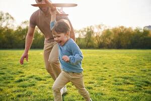 Toy,, plane in hand, running. Happy father with son are having fun on the field at summertime photo