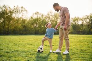 Game of ,,soccer. With ball. Happy father with son are having fun on the field at summertime photo