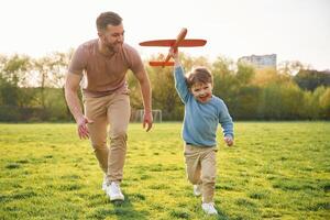 Toy, plane in hand, running. Happy father with son are having fun on the field at summertime photo